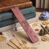 Redwood plum blossom bookmark displayed against vintage stack of books and ancient letters with porcelain bead accent.