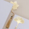 Gold metal hollow maple and gingko leaf bookmarks placed inside an open vintage book on a beige linen surface.