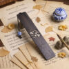 Dark wooden bookmark with carved bamboo pattern resting on vintage manuscripts with calligraphy brush and inkpot.