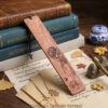 Natural wood orchid bookmark leaned against classic leather books surrounded by calligraphy paper and ginkgo leaves.