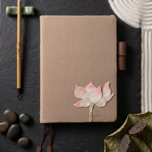 Handcrafted light taupe linen A5 book cover with pink lotus embroidery on black slate stone surrounded by zen sand art